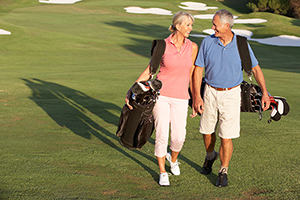 Senior Couple Walking Along Golf Course Carrying Bags atheletes with Carpal Tunnel
