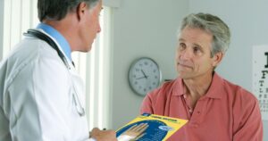 Doctor speaks with an older man holding a Carpal Solution package in a clinic.