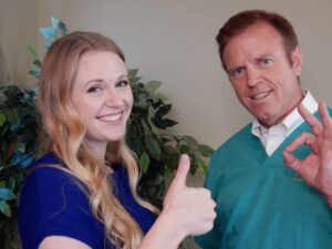 Smiling woman gives a thumbs up while a man in teal scrubs makes an OK sign.