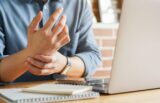 Person holding a sore wrist while working at a laptop on a desk