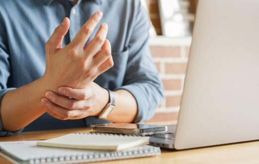 Person holding a sore wrist while working at a laptop on a desk