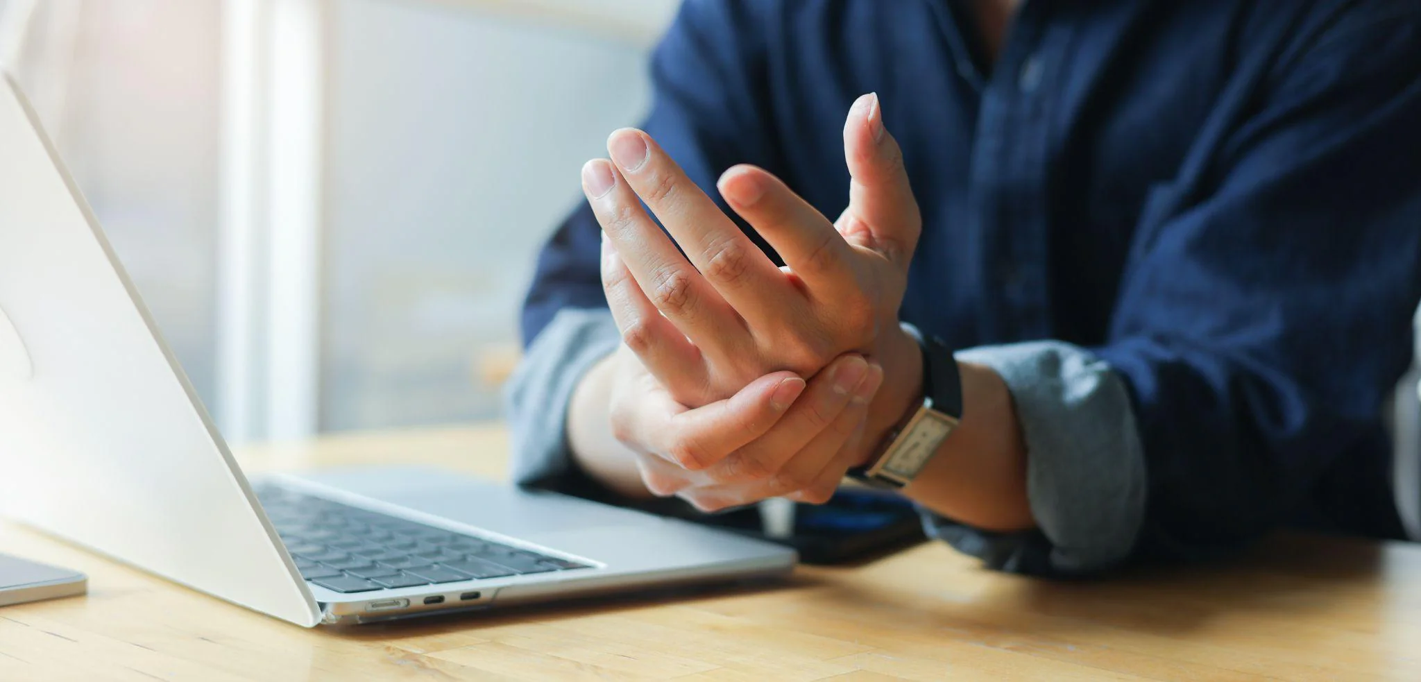 Person holding their wrist beside a laptop, suggesting hand or wrist discomfort. carpal tunnel go away on its own
